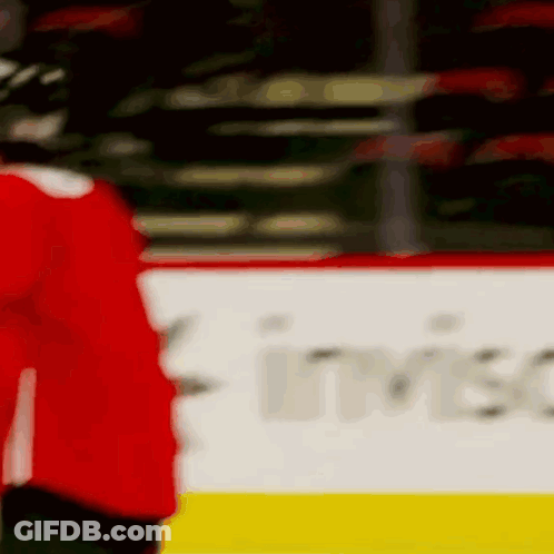 A Hockey Player In A Red Jersey Is Standing On The Ice In Front Of A Banner . GIF