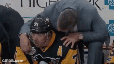 A Hockey Player Is Being Helped By A Man In A Suit While Sitting On A Bench . GIF