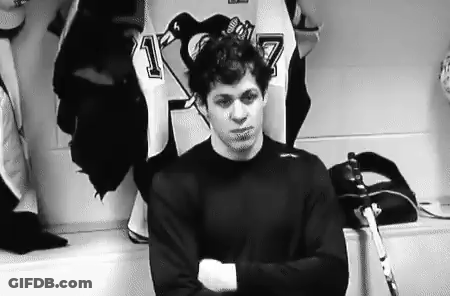 A Hockey Player Is Standing In A Locker Room With His Arms Crossed And A Hockey Stick . GIF