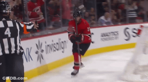 A Hockey Player Stands On The Ice With A Referee In Front Of A Banner That Says Invisalign GIF