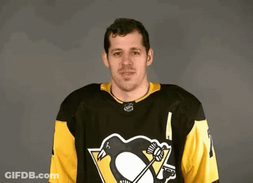 A Hockey Player Wearing A Black And Yellow Jersey With A Penguin On It Is Standing In Front Of A Gray Background . GIF