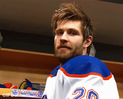 A Hockey Player With The Number 20 On His Jersey Stands In A Locker Room GIF