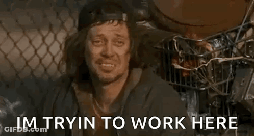 A Homeless Man Is Sitting In Front Of A Chain Link Fence And Says `` Im Tryin To Work Here '' . GIF