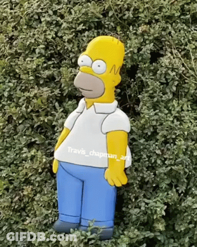 A Homer Simpson Statue Is Standing In A Bush GIF