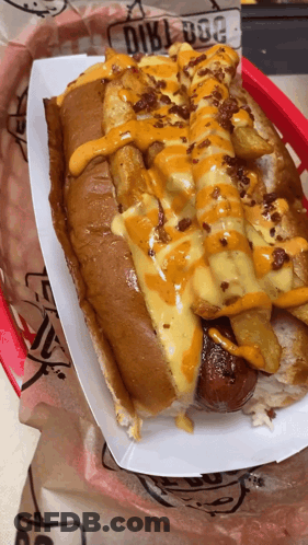 A Hot Dog With Cheese And French Fries Is In A Paper Container GIF