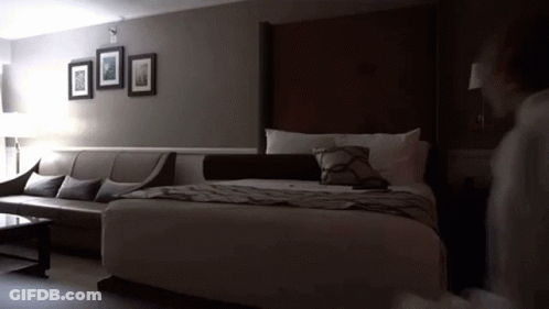 A Hotel Room With A King Size Bed A Couch And A Coffee Table GIF