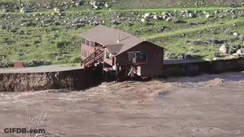 A House Sits In The Middle Of A River Surrounded By Grass And Rocks GIF
