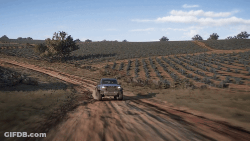 A Jeep Is Driving Down A Dirt Road With A Field In The Background GIF