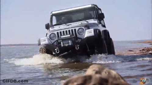 A Jeep Is Driving Through A Body Of Water With A Few Rocks In The Foreground GIF