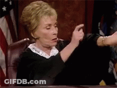 A Judge Is Sitting At A Table In A Courtroom Pointing At Someone . GIF