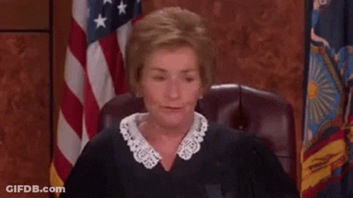 A Judge Is Sitting In A Courtroom With An American Flag In The Background . GIF