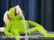 A Kermit The Frog Is Laying On A Bed With A Stuffed Animal And Says `` Disgusting '' . GIF