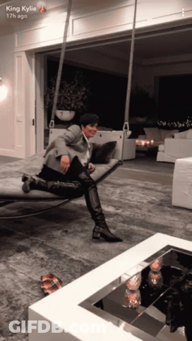 A King Kylie Snapchat Shows A Woman Sitting On A Swing In A Living Room GIF