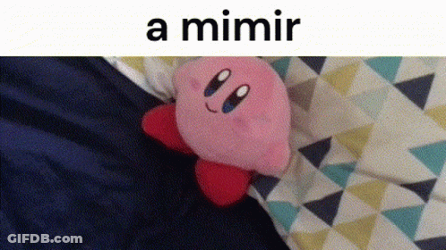 A Kirby Stuffed Animal Is Laying On A Bed Next To A Triangle Patterned Blanket . GIF