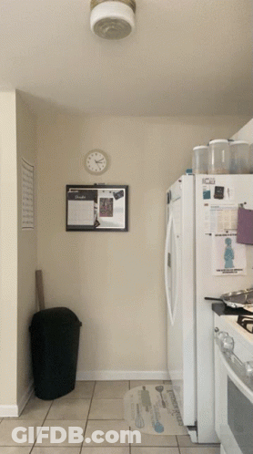 A Kitchen With A Clock On The Wall Above The Refrigerator And A Bulletin Board On The Wall GIF