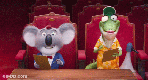 A Koala And A Lizard Are Sitting At A Table In A Theater GIF