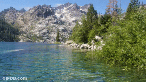 A Lake With Mountains In The Background Is Surrounded By Trees And Rocks GIF