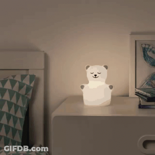 A Lamp In The Shape Of A Polar Bear Sits On A Nightstand In Front Of A Bed GIF