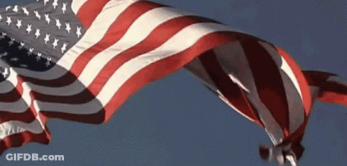 A Large American Flag Is Flying In The Wind GIF
