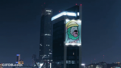 A Large Billboard On The Side Of A Building Has A Picture Of A Man With A Beard And Hat On It GIF