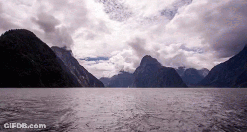 A Large Body Of Water Surrounded By Mountains And A Cloudy Sky GIF