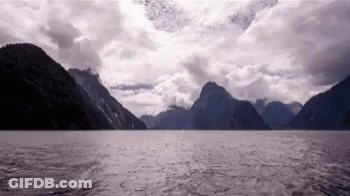 A Large Body Of Water Surrounded By Mountains And Clouds GIF