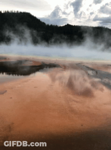 A Large Body Of Water With Mountains In The Background And Smoke Coming Out Of The Water GIF