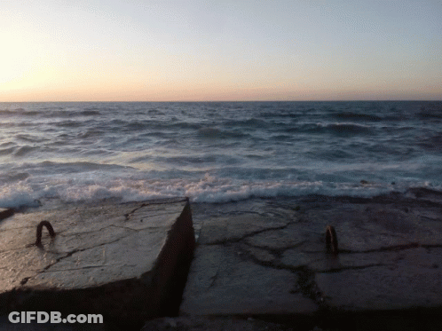 A Large Body Of Water With Waves Crashing On A Rocky Shoreline GIF