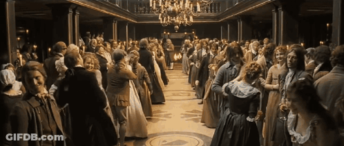 A Large Crowd Of People Are Dancing In A Ballroom With A Chandelier GIF