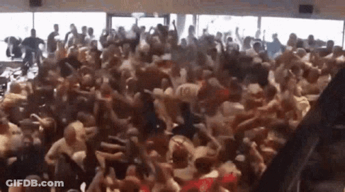 A Large Crowd Of People Are Dancing In A Room With A Lot Of Windows . GIF
