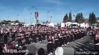 A Large Crowd Of People Are Gathered In A Parade . GIF