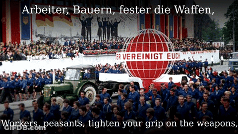 A Large Crowd Of People Are Gathered In Front Of A Sign That Says " Arbeiter Bauern Fester Die Waffen " GIF