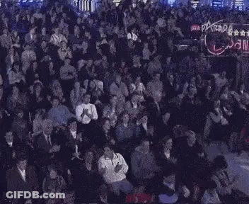 A Large Crowd Of People Are Sitting In A Dark Room With The Word Parada On The Bottom GIF