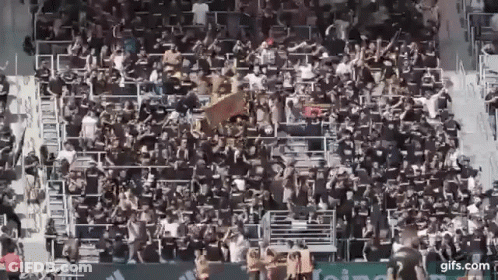 A Large Crowd Of People Are Sitting In A Stadium Watching A Soccer Game . GIF