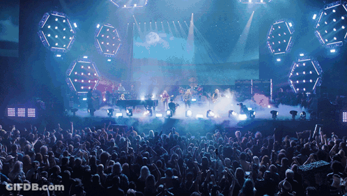 A Large Crowd Of People Are Watching A Band On Stage GIF
