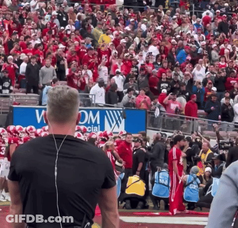 A Large Crowd Of People Watching A Football Game In Front Of A Sign That Says Wom GIF