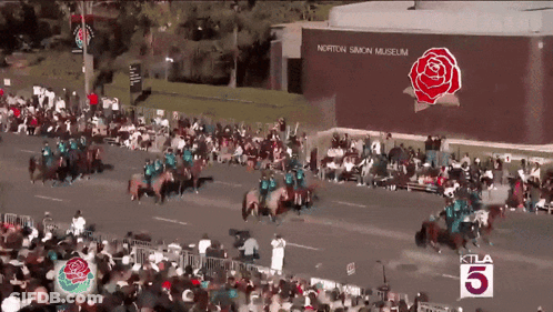 A Large Crowd Of People Watching A Parade In Front Of A Building That Says Norton Simon Museum GIF