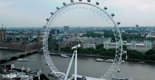 A Large Ferris Wheel In The Middle Of A City With The Olympics Logo On The Bottom GIF