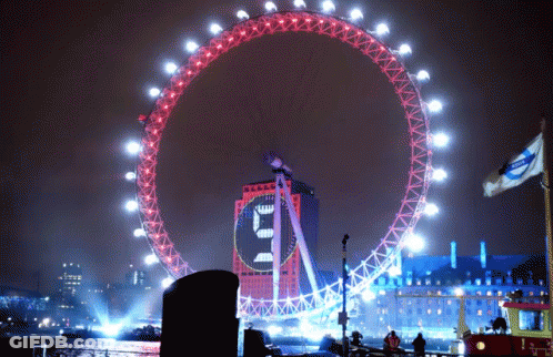 A Large Ferris Wheel Is Lit Up At Night And Has A Clock On It That Says ' E ' On It GIF