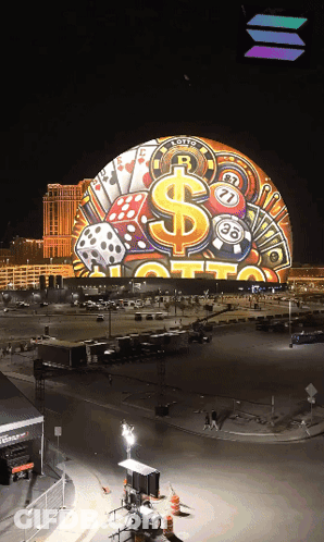 A Large Globe With A Dollar Sign Dice And Playing Cards On It Is Lit Up At Night GIF