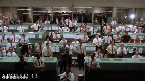 A Large Group Of Men Are Gathered In A Room With The Words Apollo 13 On The Bottom Right GIF