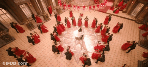 A Large Group Of People Are Dancing In A Room With A Chandelier GIF