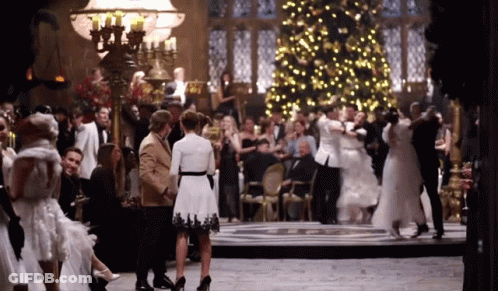 A Large Group Of People Are Dancing In A Room With A Christmas Tree In The Background GIF