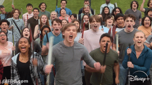 A Large Group Of People Are Holding Bats And Screaming In Front Of A Disney+ Logo GIF