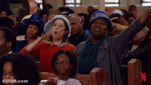 A Large Group Of People Are Sitting In A Church With Their Hands In The Air . GIF