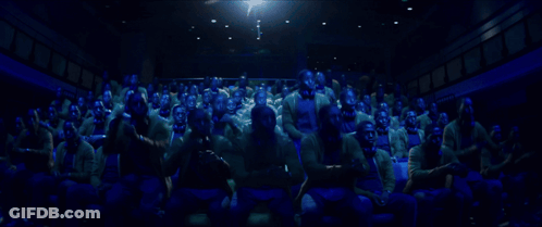 A Large Group Of People Are Sitting In A Dark Auditorium Watching A Movie GIF