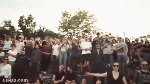 A Large Group Of People Are Standing In A Stadium With Their Arms In The Air . GIF