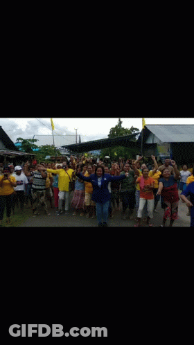 A Large Group Of People Are Standing In Front Of A Building Holding Their Hands Up In The Air . GIF