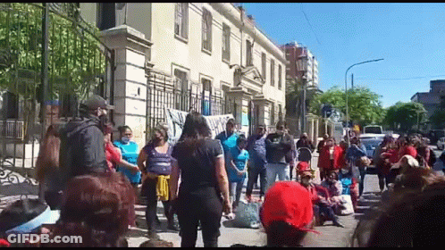 A Large Group Of People Are Standing In Front Of A Building On A Street . GIF