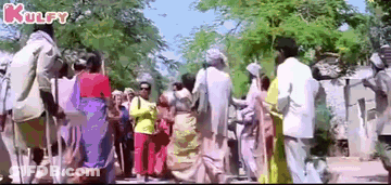 A Large Group Of People Are Walking Down A Street In A Village . GIF